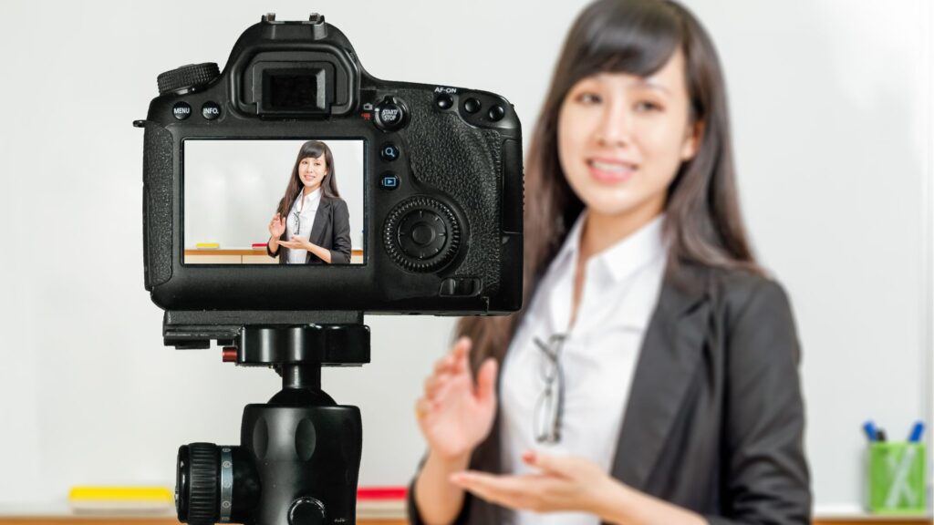 A professional woman wearing headphones, sitting at a desk and confidently recording a video using her smartphone on a small tripod.